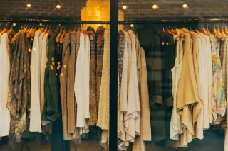 Garments on wooden hangers fill a clothing shop display behind a glass window.
