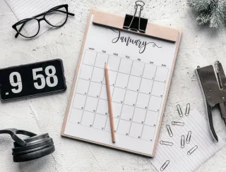 A January calendar on a clipboard beside a clock, pencil and desk stationery.