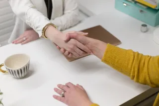 Two people shaking hands over a work table
