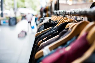 Clothing on wooden hangers along a shop display rail, with the store interior blurred behind it.