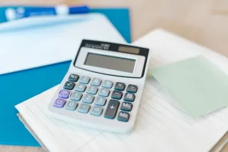 A white calculator rests on lined pages and a blue folder.