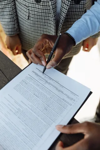 A hand signing a printed contract with a pen.
