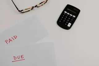 A calculator and eyeglasses beside financial papers marked paid and due.