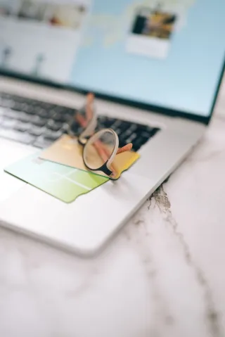 Two bank cards and eyeglasses resting on a laptop below its screen.