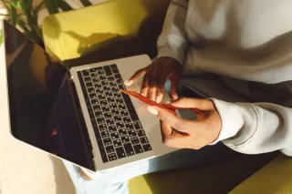 A person holding a bank card while using a laptop on their lap.
