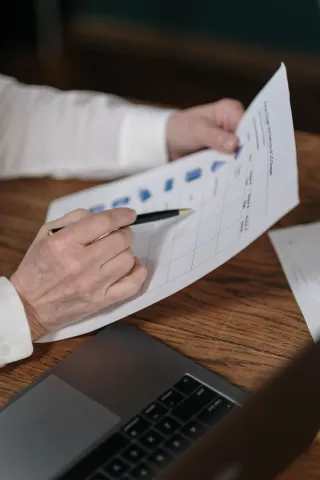 Hands hold a pen and printed financial report above a wooden desk and laptop.