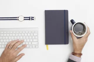 A person working beside a laptop and notebook