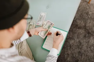 A person holds dollar-denominated notes while writing in a weekly planner.