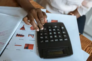A hand operates a desktop calculator above printed financial charts.